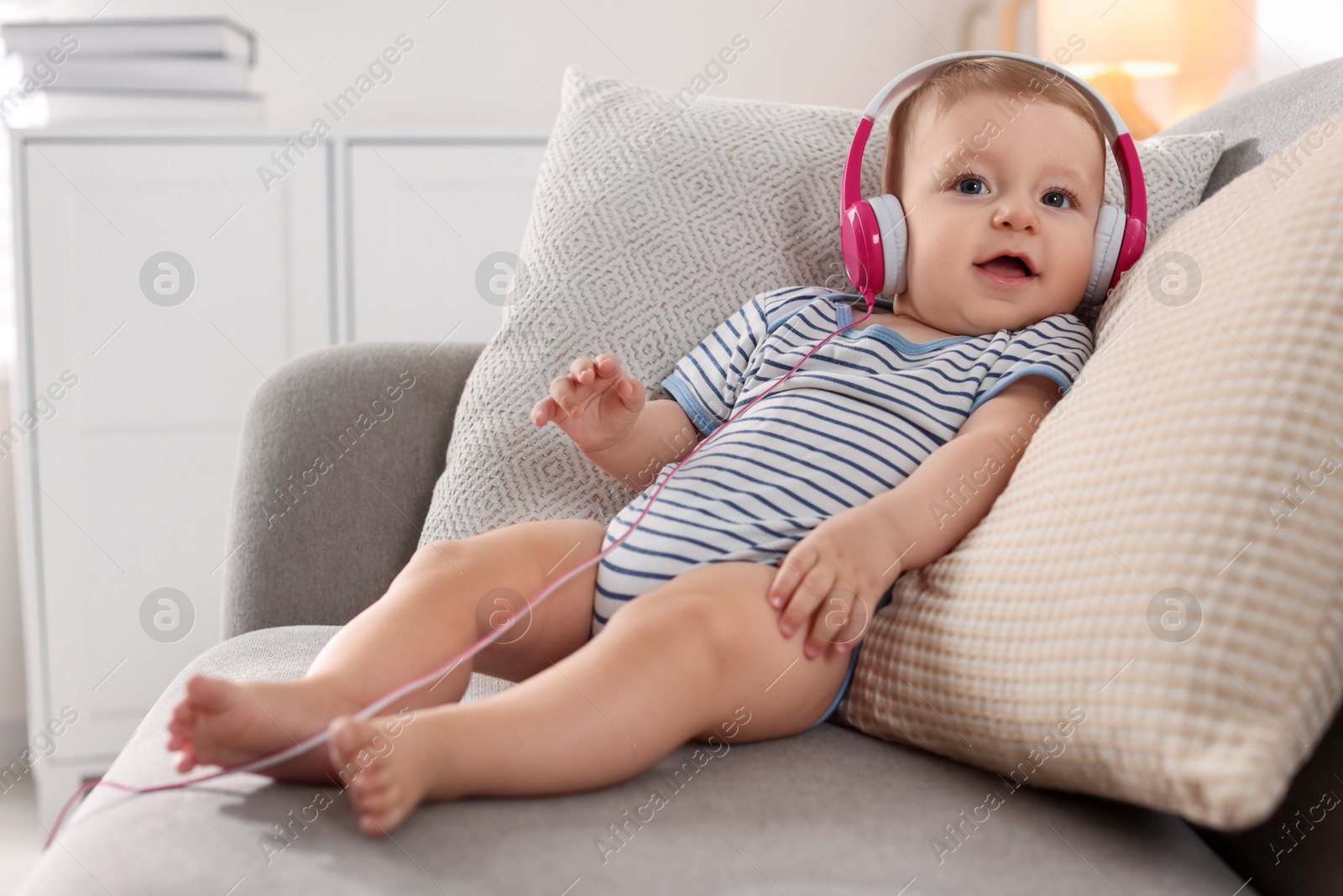 Photo of Cute little baby with headphones on sofa at home