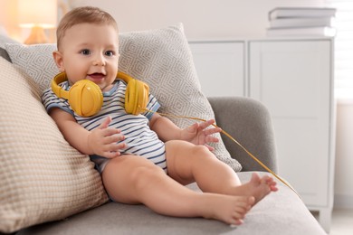 Cute little baby with headphones on sofa at home, space for text