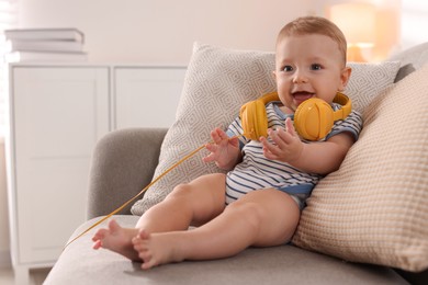 Cute little baby with headphones on sofa at home, space for text