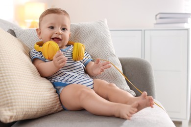 Cute little baby with headphones on sofa at home, space for text