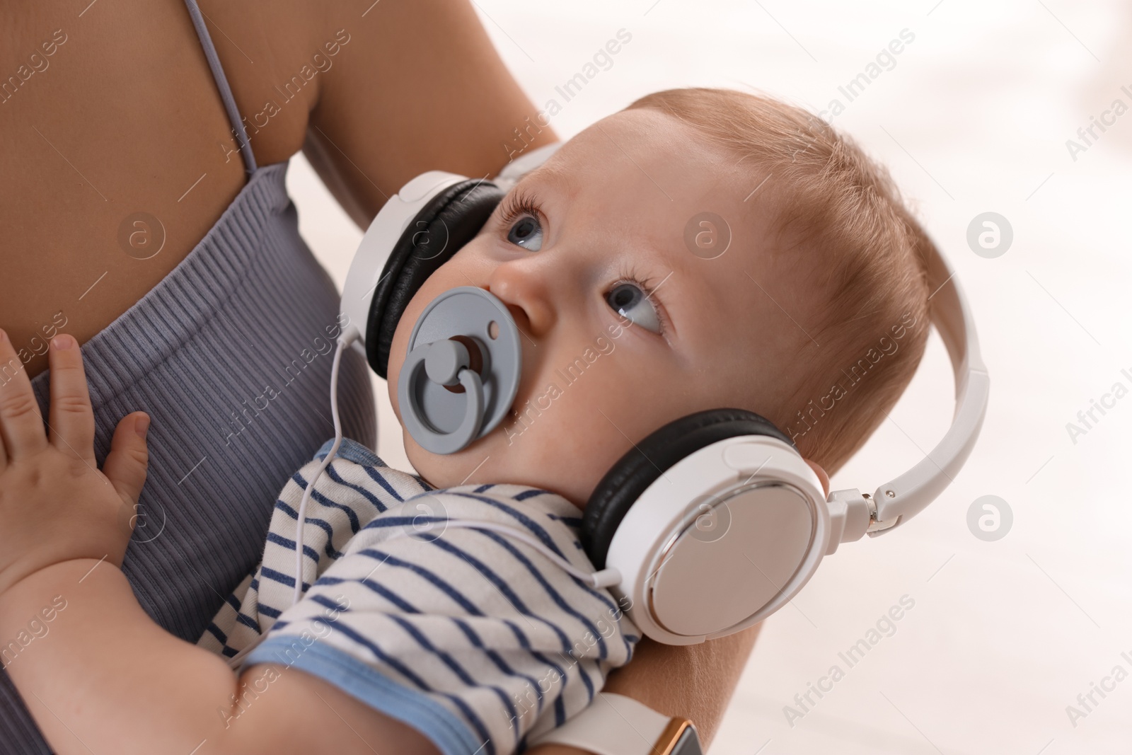 Photo of Mother holding her cute little baby with headphones and pacifier at home, closeup