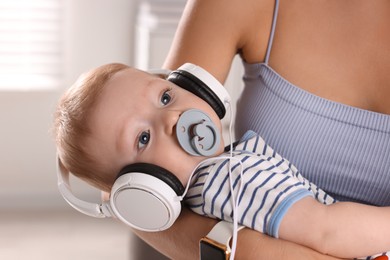 Mother holding her cute little baby with headphones and pacifier at home, closeup