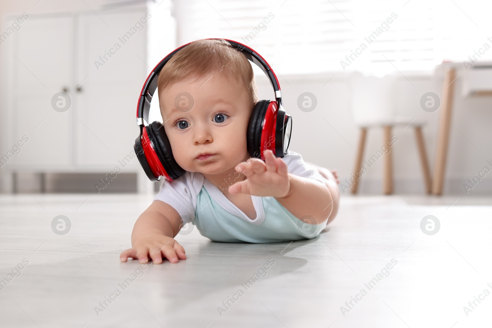 Photo of Cute little baby with headphones on floor at home