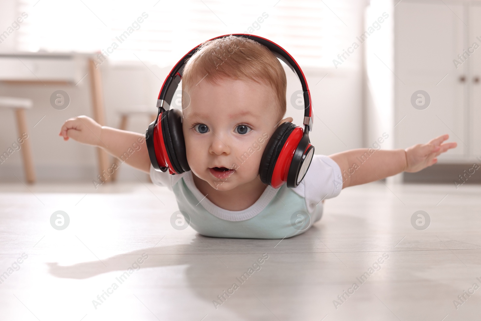 Photo of Cute little baby with headphones on floor at home