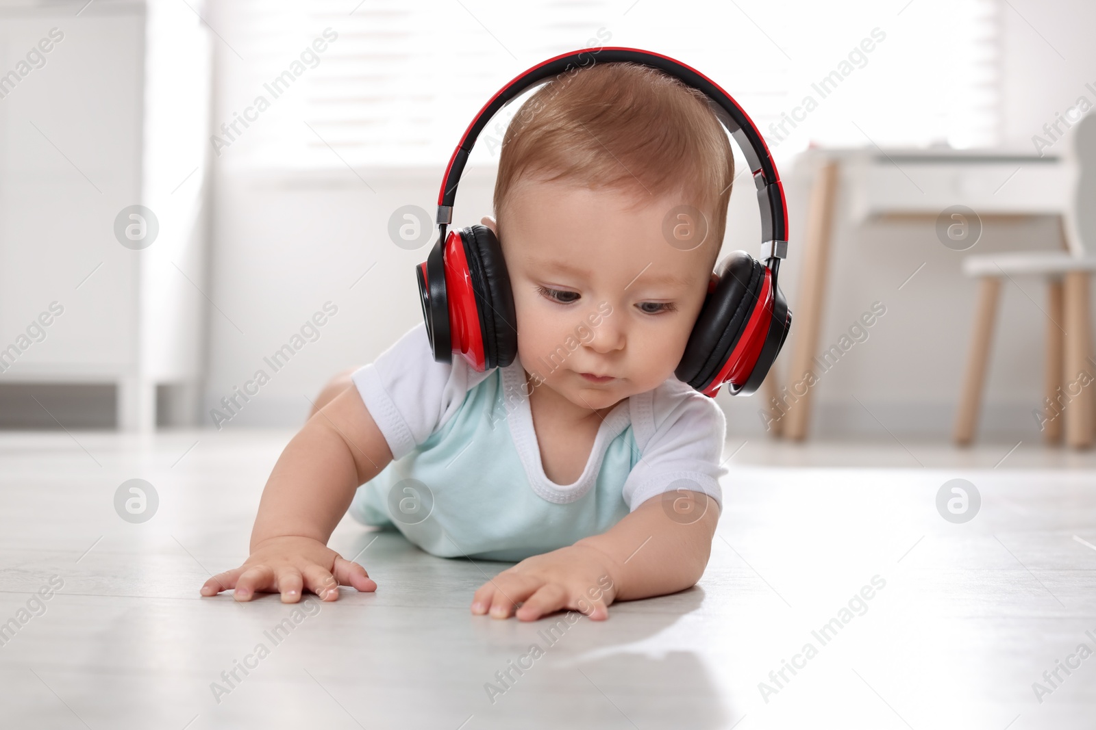 Photo of Cute little baby with headphones on floor at home