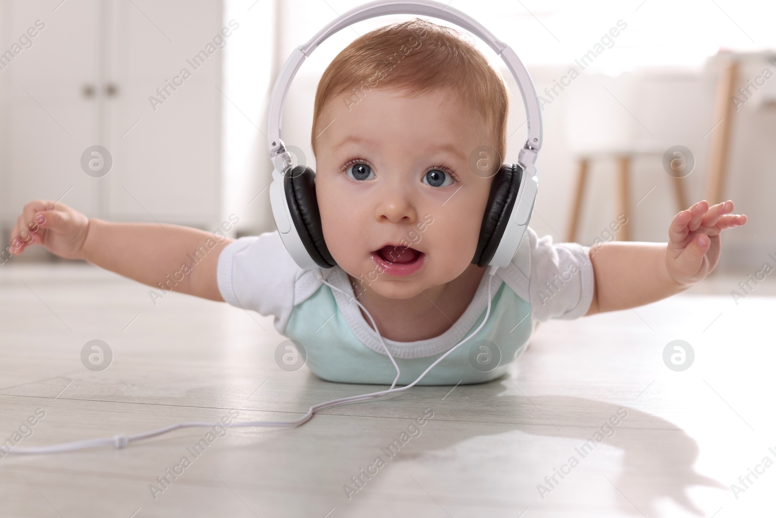 Photo of Cute little baby with headphones on floor at home