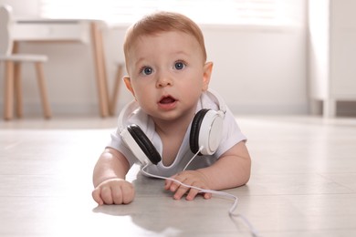 Photo of Cute little baby with headphones on floor at home