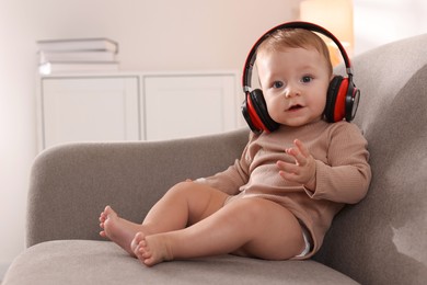 Cute little baby with headphones on sofa at home, space for text