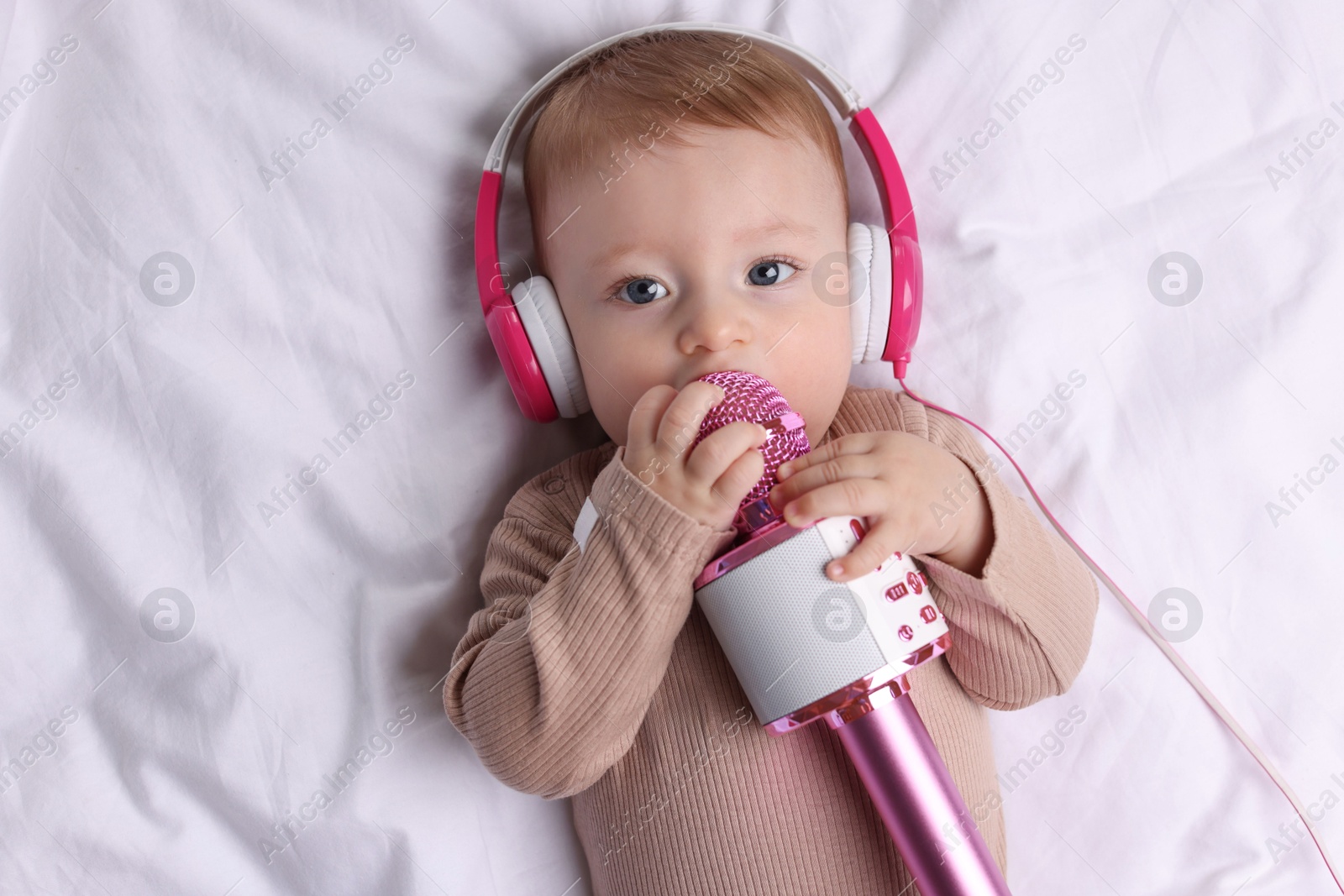 Photo of Cute little baby with headphones and microphone lying on bed, top view