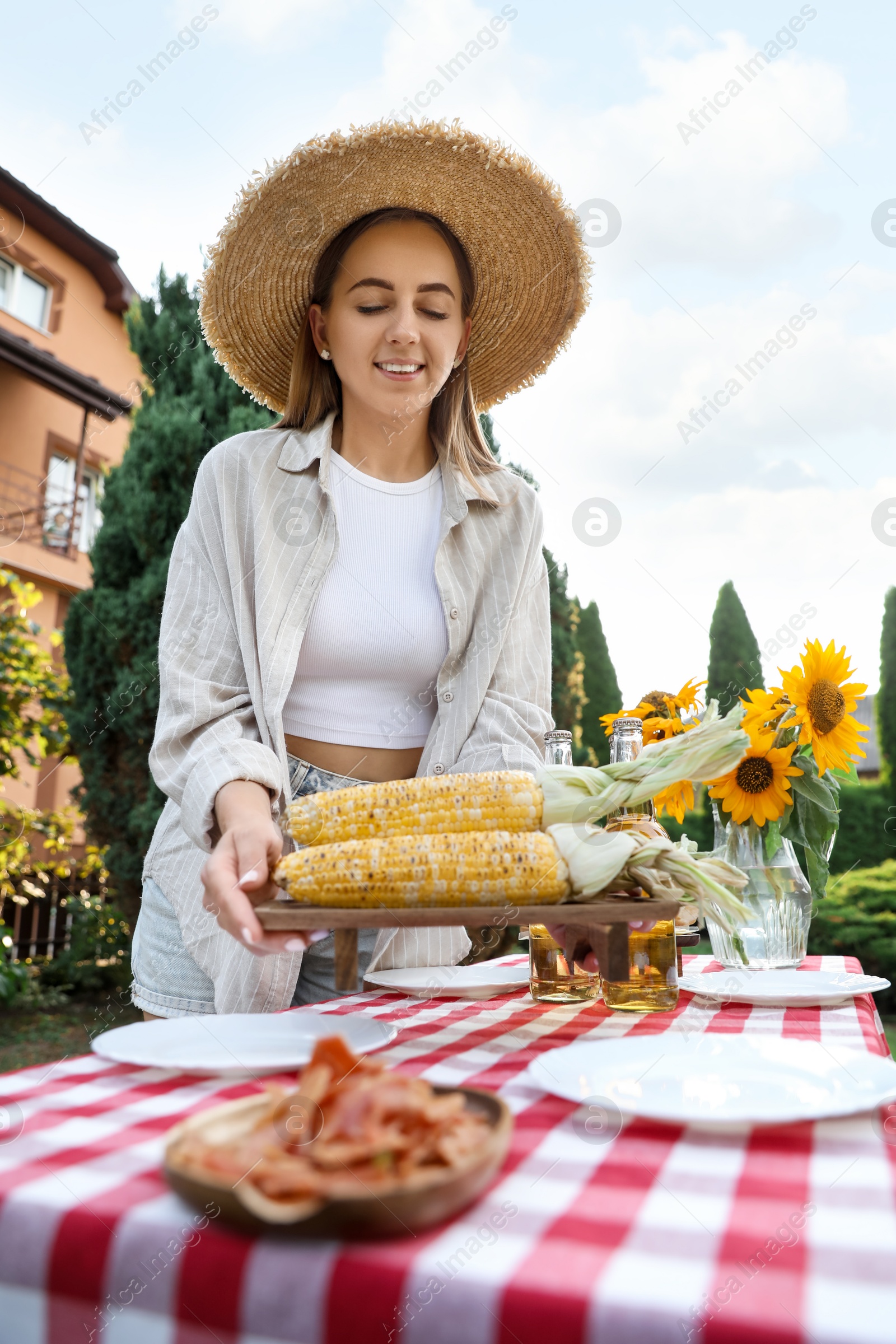 Photo of Beautiful woman with fresh corncobs near table in garden