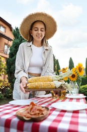 Beautiful woman with fresh corncobs near table in garden