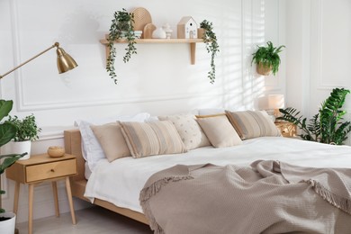 Photo of Stylish bedroom interior with large bed, houseplants and decorative elements