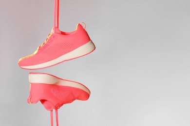 Photo of Pair of stylish sneakers in air against light grey background in neon lights, space for text