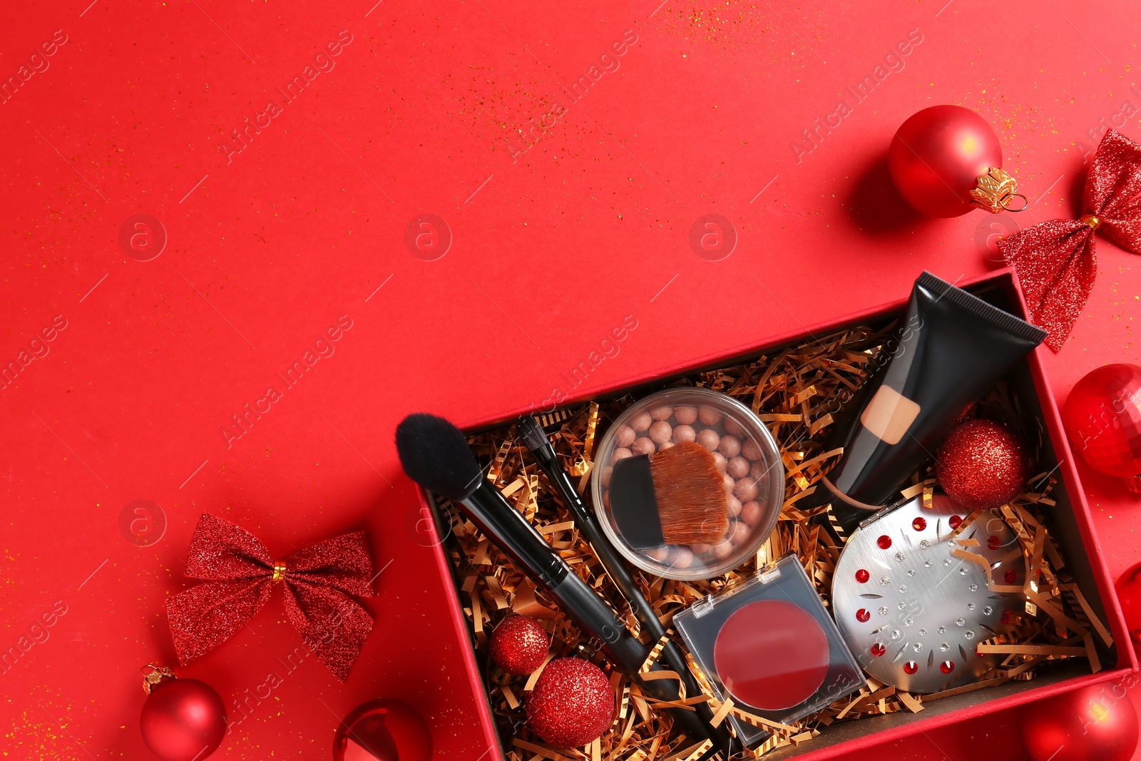 Photo of Christmas gift box with cosmetic products and festive decor on red background, top view. Space for text