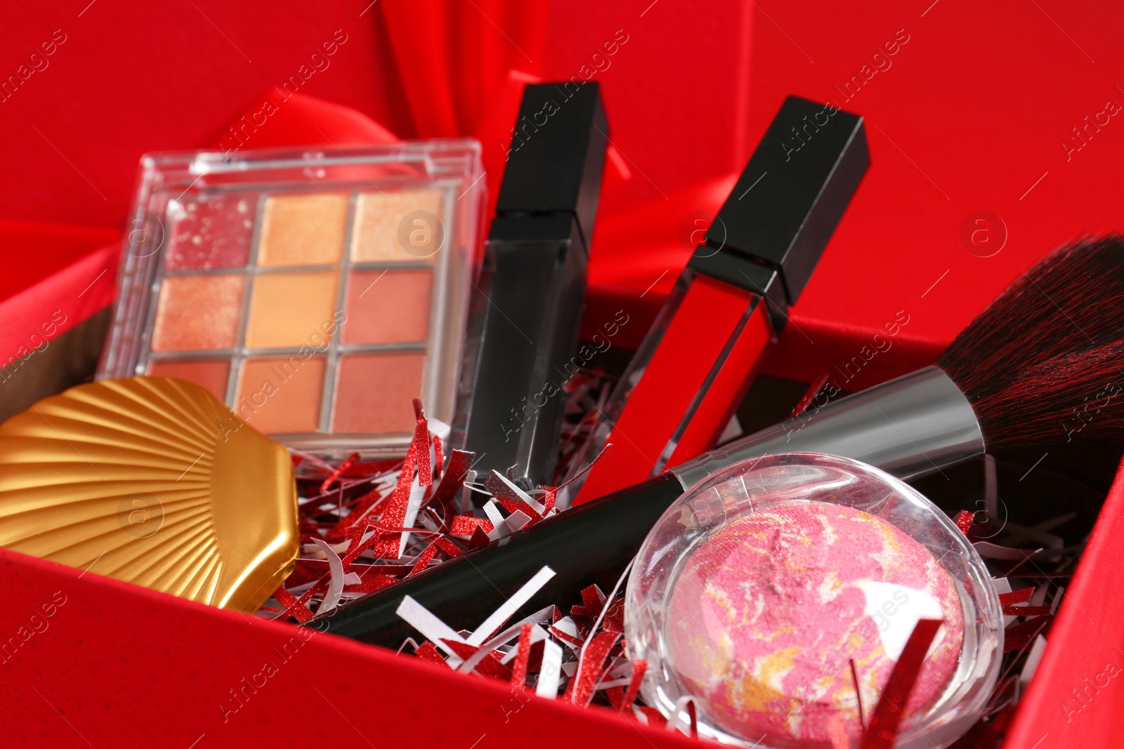 Photo of Christmas gift box with cosmetic products on red background, closeup