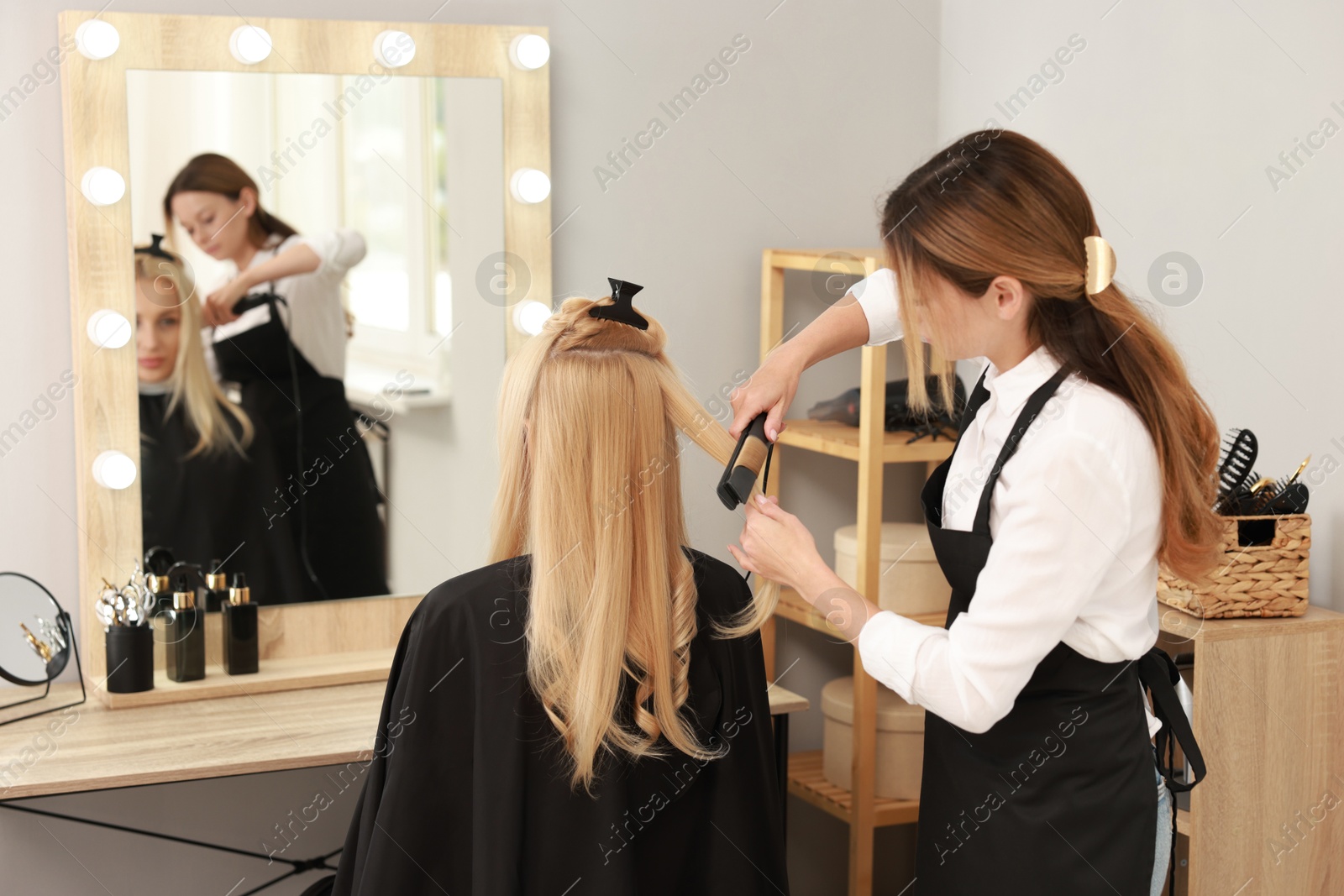 Photo of Hairdresser curling woman's hair with flat iron in salon