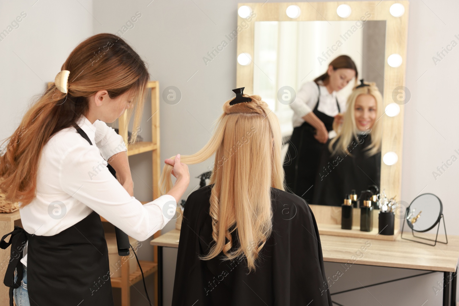 Photo of Hairdresser curling woman's hair with flat iron in salon