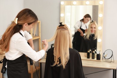 Hairdresser curling woman's hair with flat iron in salon