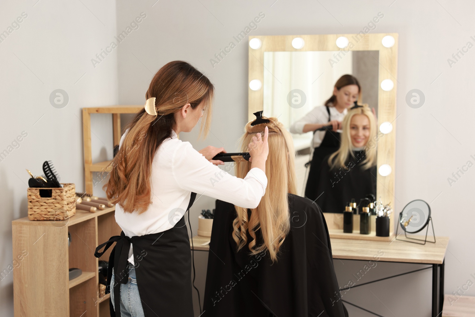 Photo of Hairdresser curling woman's hair with flat iron in salon