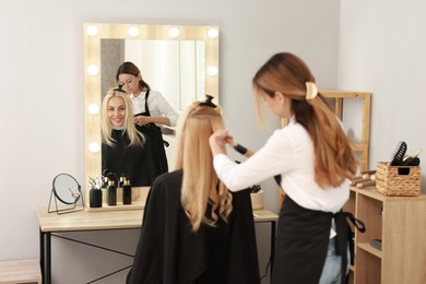 Photo of Hairdresser curling woman's hair with flat iron in salon