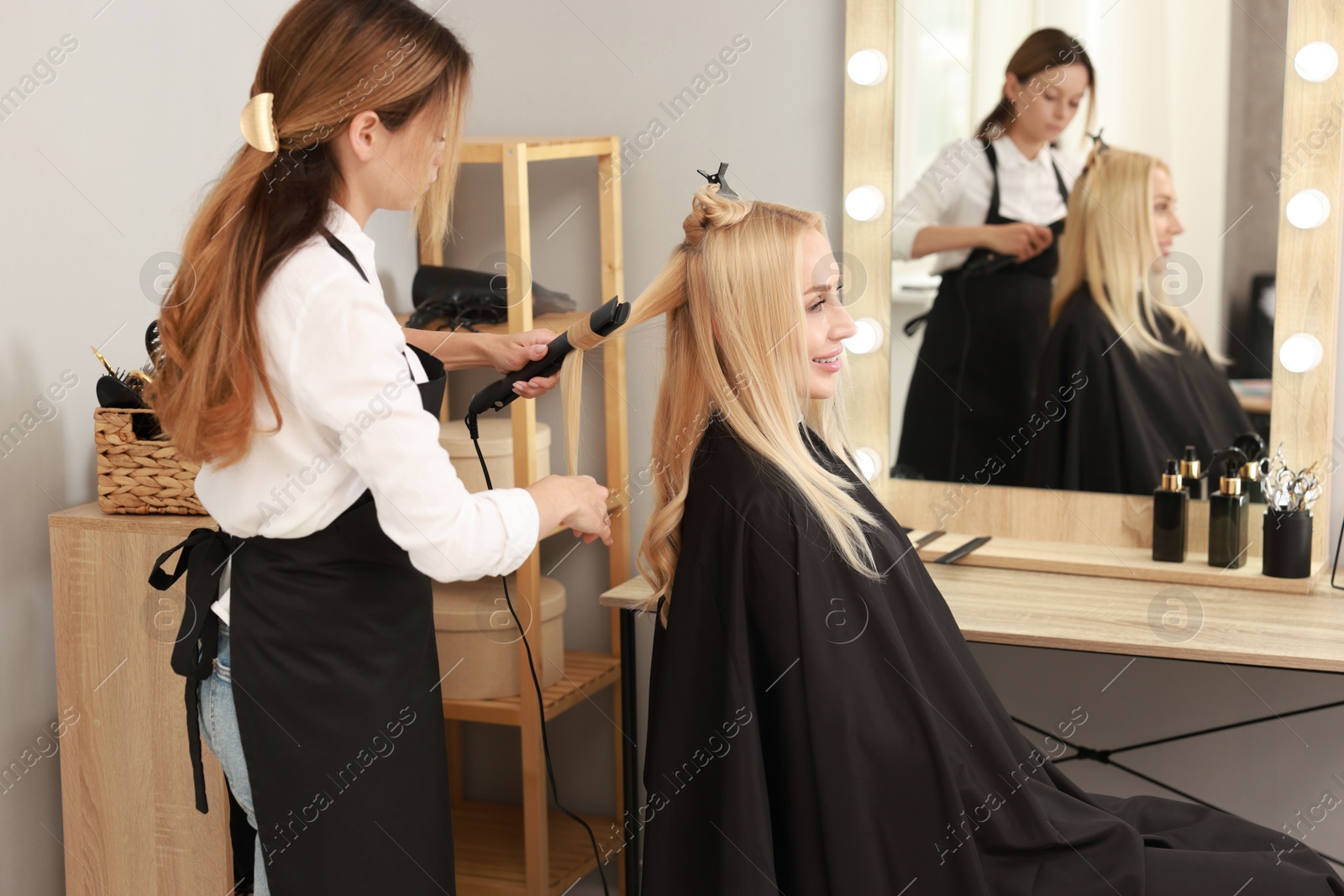 Photo of Hairdresser curling woman's hair with flat iron in salon