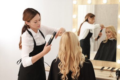 Photo of Hairdresser curling woman's hair with flat iron in salon