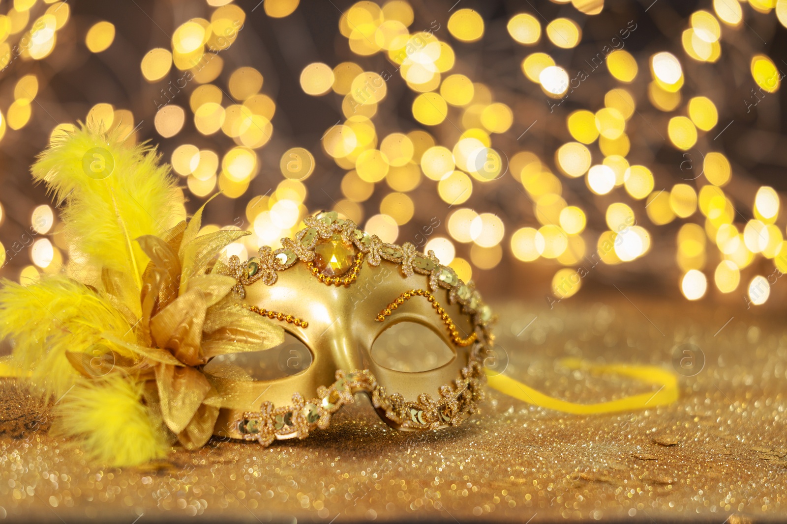 Photo of Beautiful carnival mask on golden shiny background, space for text. Bokeh effect