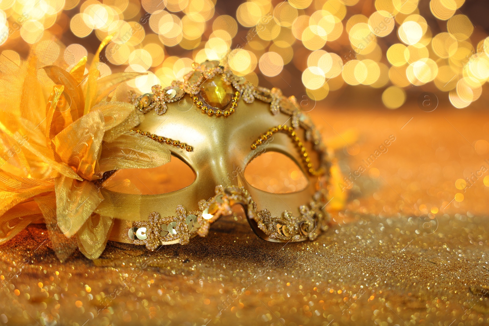 Photo of Beautiful carnival mask on golden shiny background, space for text. Bokeh effect