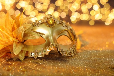 Photo of Beautiful carnival mask on golden shiny background, space for text. Bokeh effect