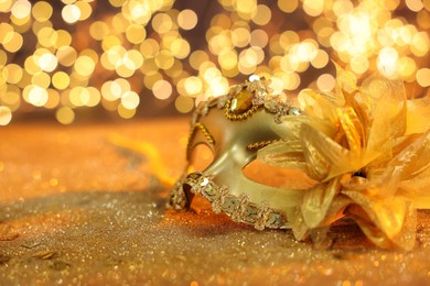 Photo of Beautiful carnival mask on golden shiny background, space for text. Bokeh effect