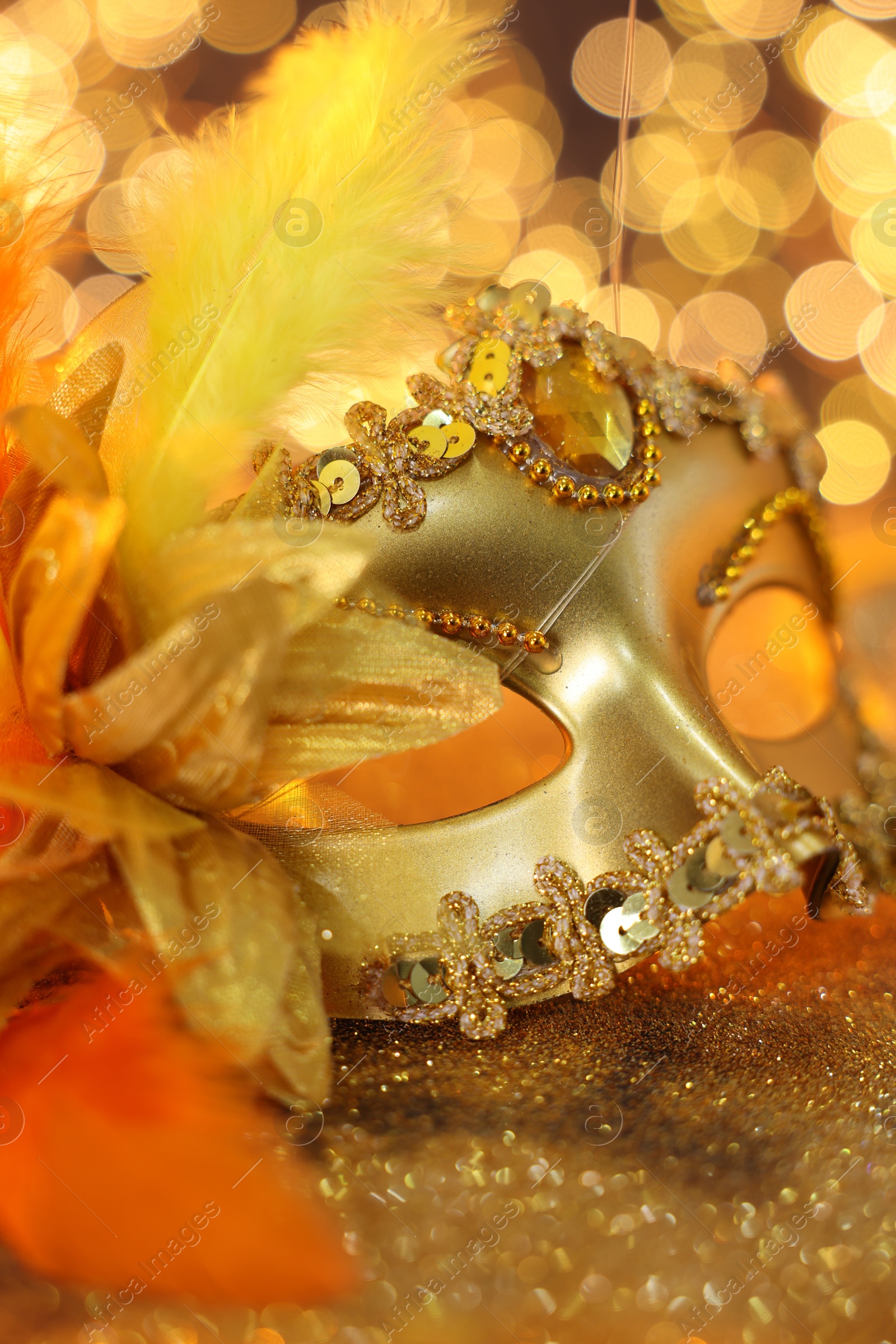 Photo of Beautiful carnival mask on golden shiny background, closeup. Bokeh effect