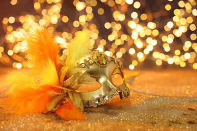 Photo of Beautiful carnival mask on golden shiny background, space for text. Bokeh effect