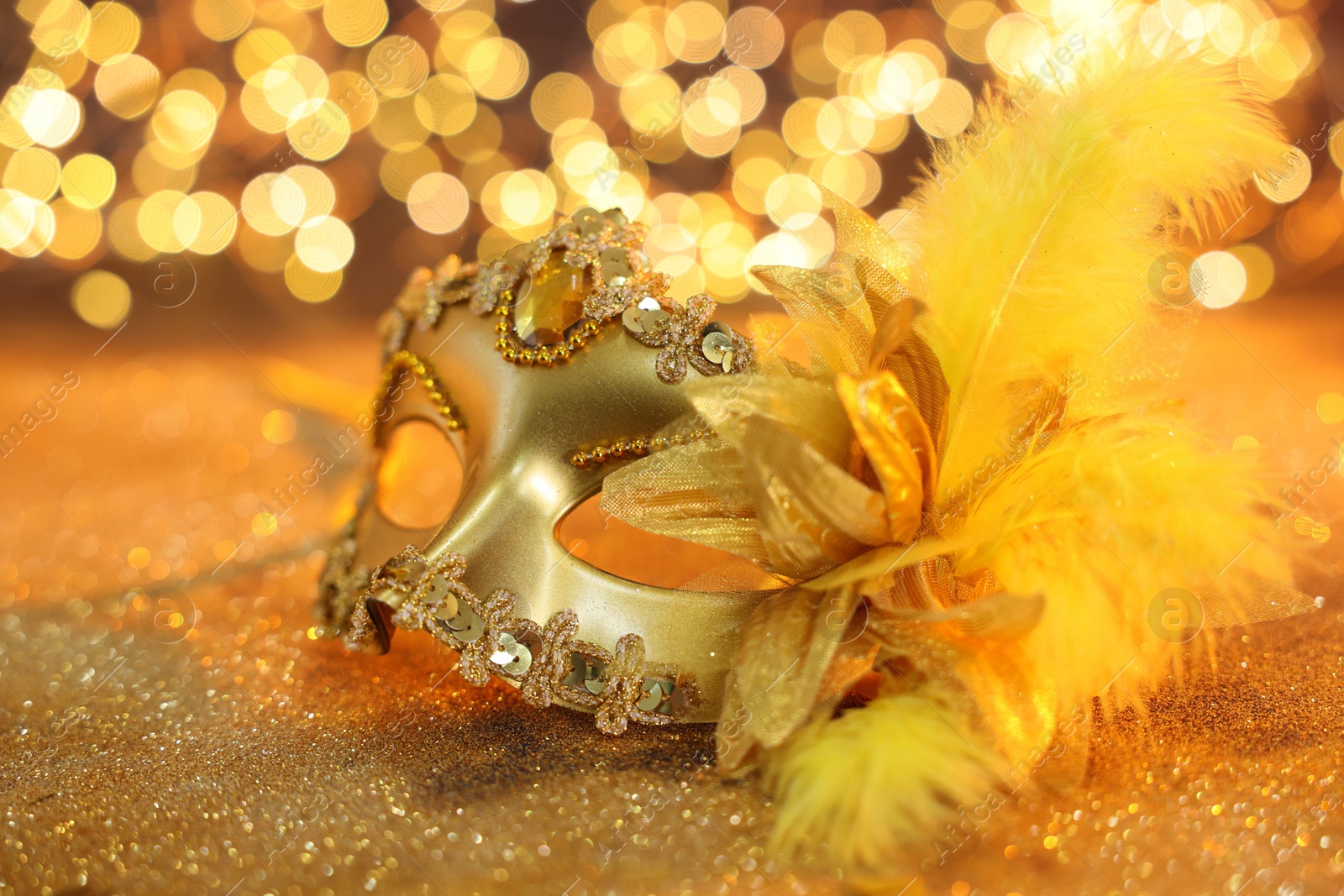 Photo of Beautiful carnival mask on golden shiny background, closeup. Bokeh effect