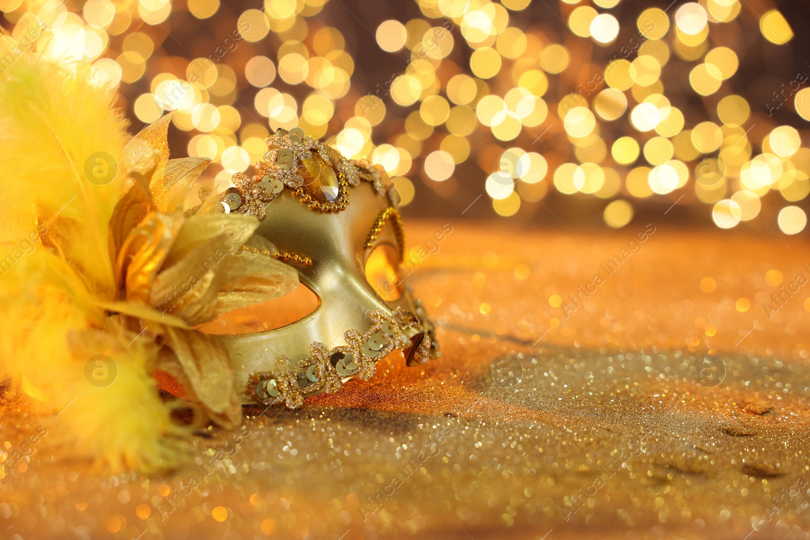 Photo of Beautiful carnival mask on golden shiny background, space for text. Bokeh effect