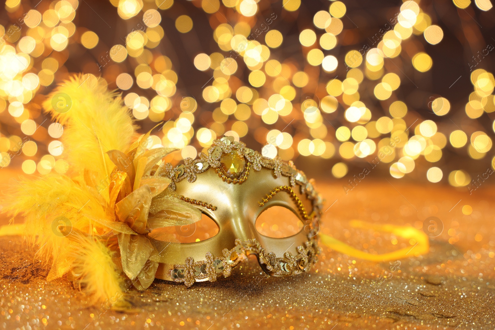 Photo of Beautiful carnival mask on golden shiny background, space for text. Bokeh effect