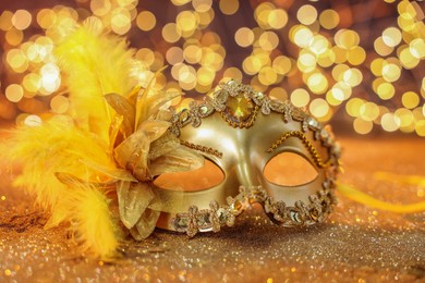 Photo of Beautiful carnival mask on golden shiny background, closeup. Bokeh effect