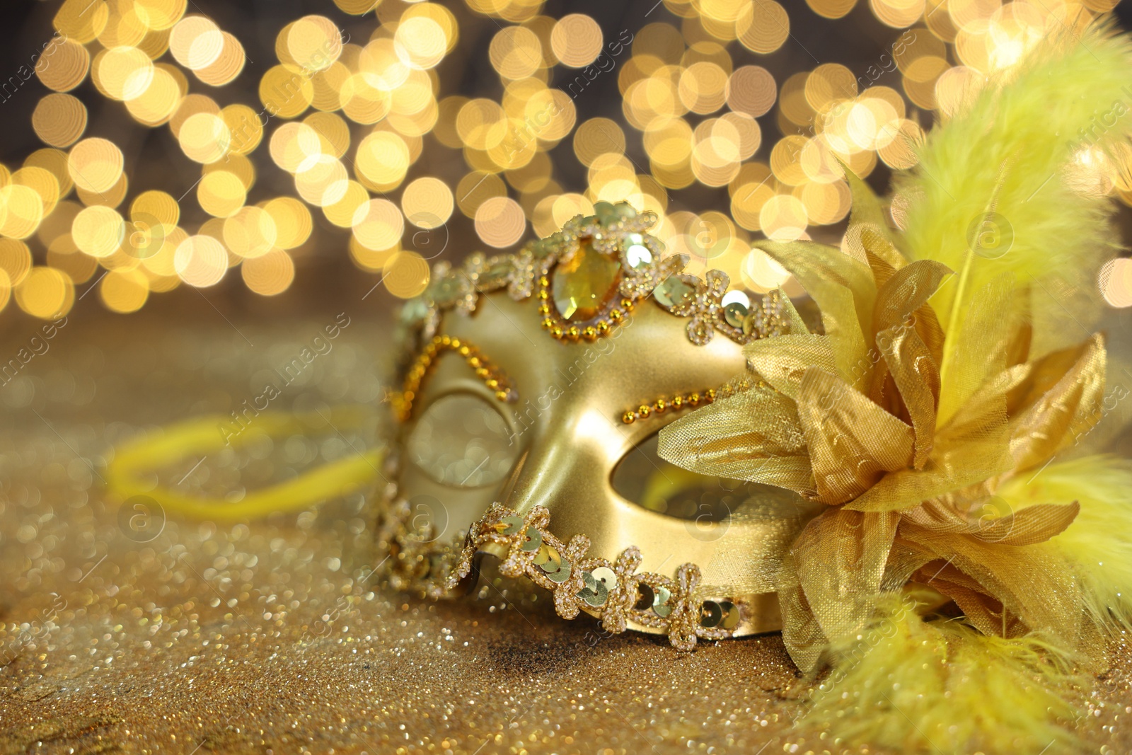 Photo of Beautiful carnival mask on golden shiny background, space for text. Bokeh effect