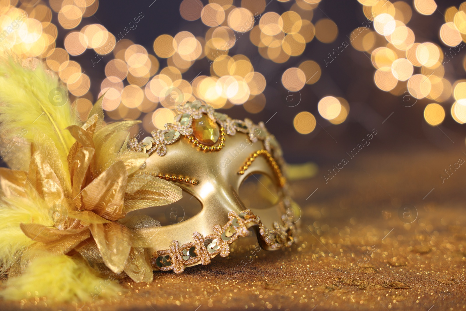 Photo of Beautiful carnival mask on golden shiny background, space for text. Bokeh effect