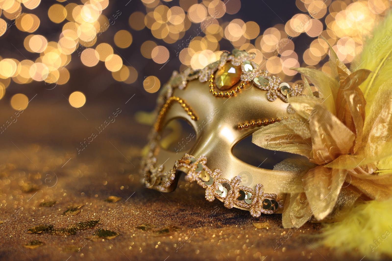 Photo of Beautiful carnival mask on golden shiny background, space for text. Bokeh effect