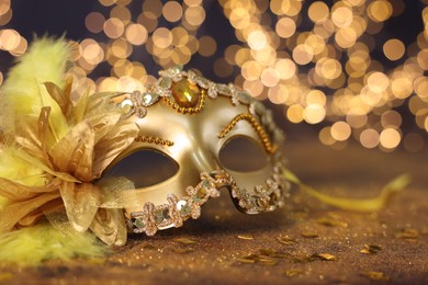 Photo of Beautiful carnival mask on golden shiny background, space for text. Bokeh effect