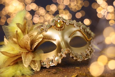 Photo of Beautiful carnival mask on golden shiny background, closeup. Bokeh effect