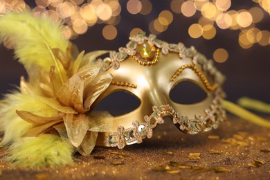 Photo of Beautiful carnival mask on golden shiny background, closeup. Bokeh effect