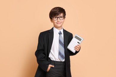 Boy with calculator pretending to be accountant on beige background. Dreaming of future profession