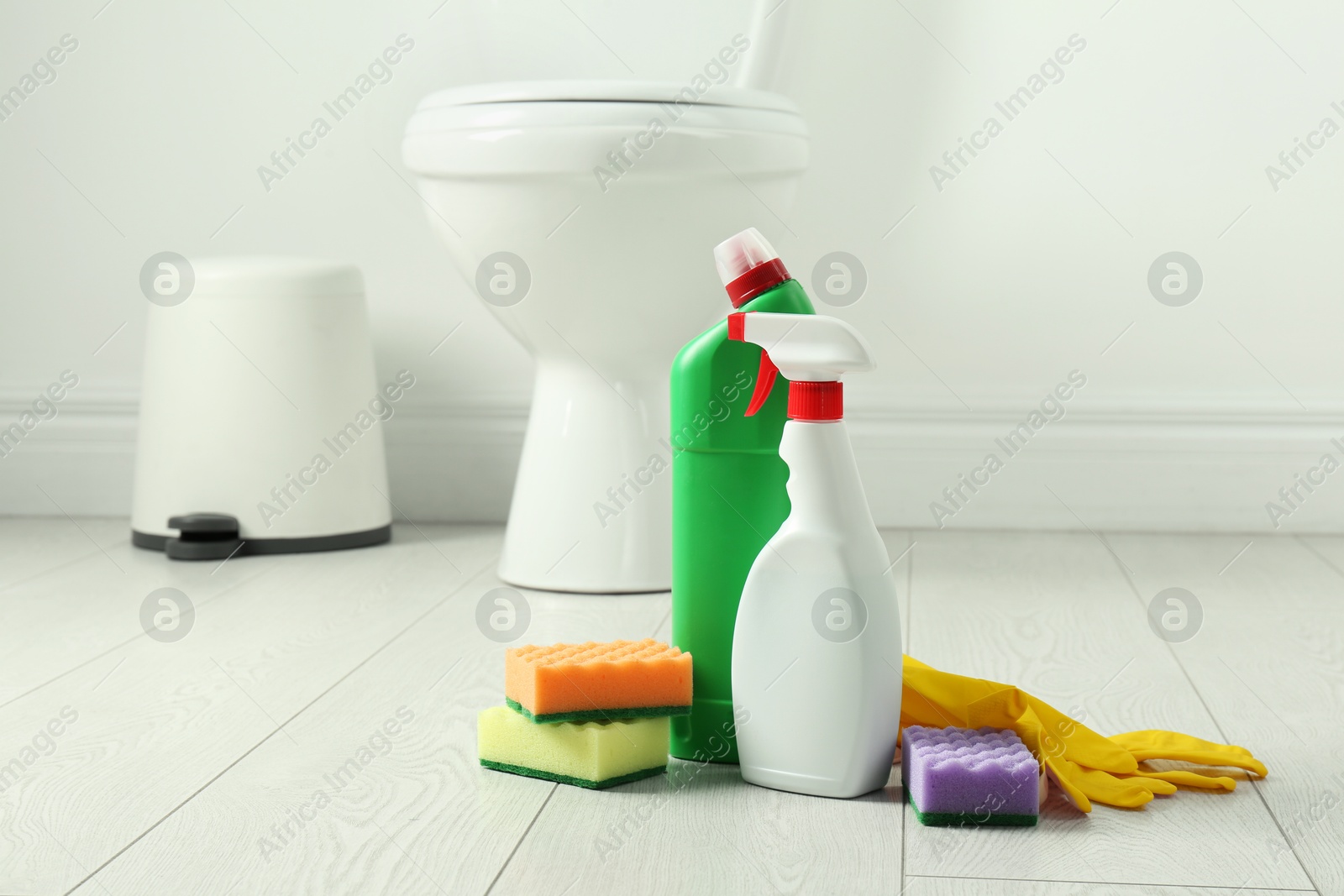 Photo of Toilet cleaners, sponges and gloves on floor in bathroom