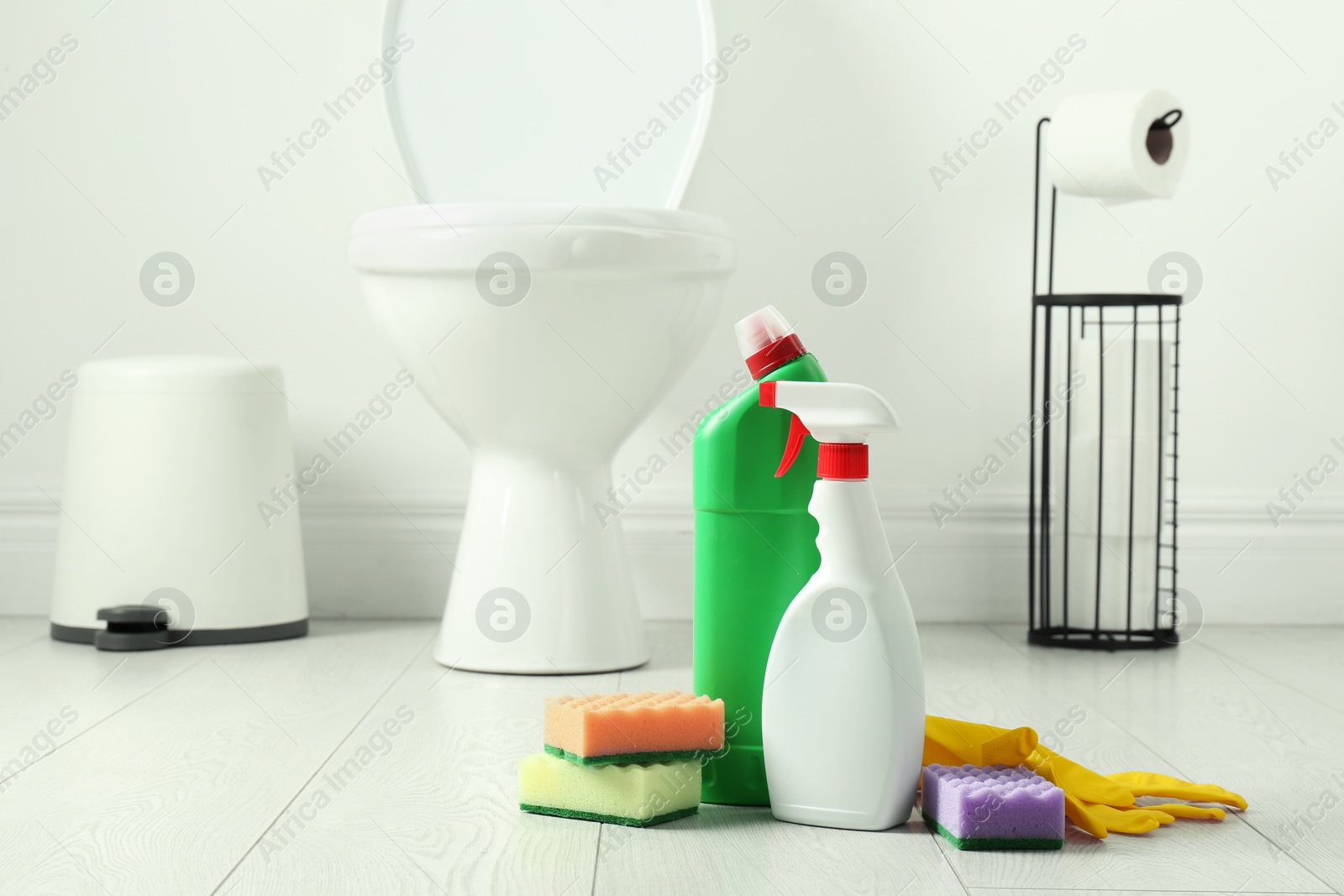 Photo of Toilet cleaners, sponges and gloves on floor in bathroom