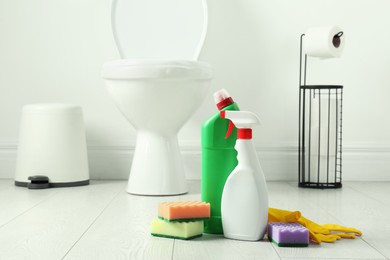 Photo of Toilet cleaners, sponges and gloves on floor in bathroom