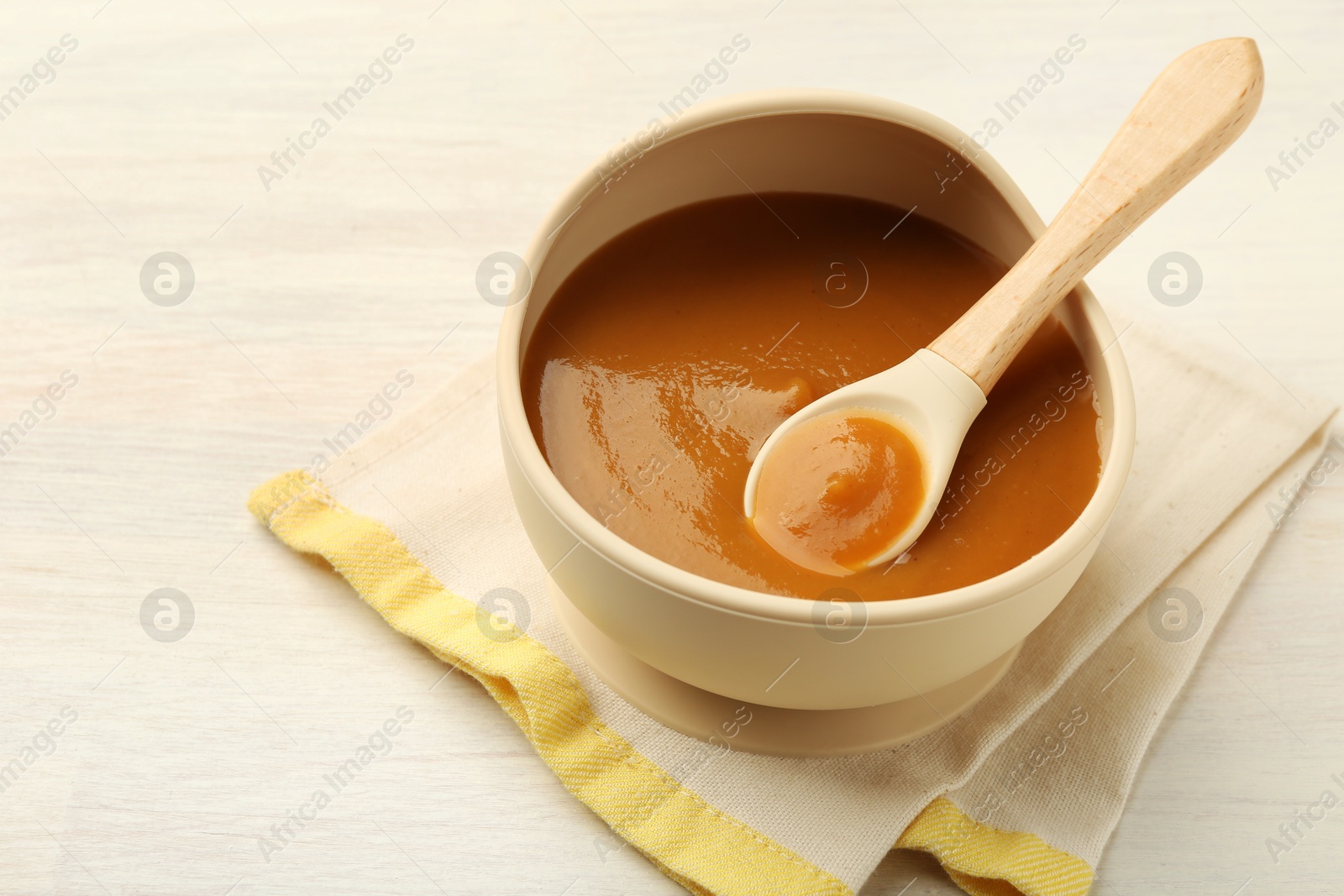 Photo of Delicious baby food with spoon in bowl on white wooden table