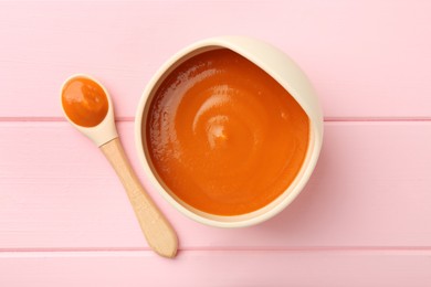 Photo of Delicious baby food in bowl and spoon on pink wooden table, flat lay