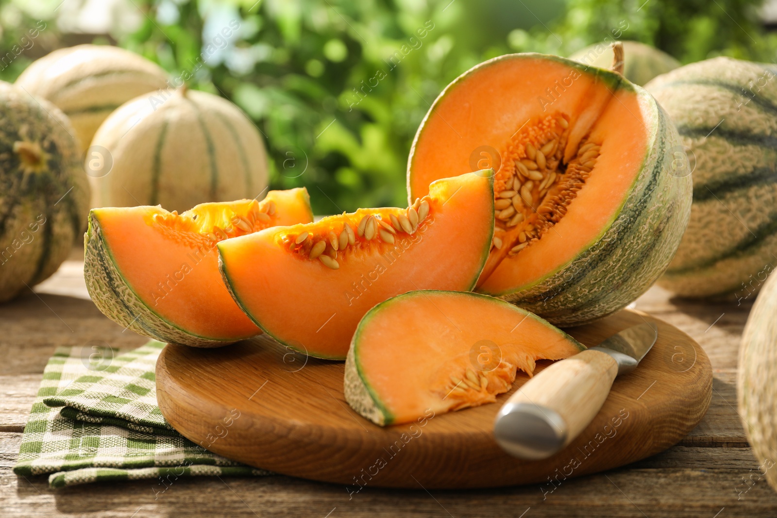 Photo of Tasty ripe Cantaloupe melons and knife on wooden table outdoors