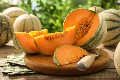 Photo of Tasty ripe Cantaloupe melons and knife on wooden table outdoors